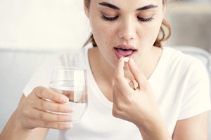 young woman taking pill with glass of water